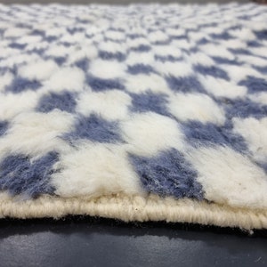 Op de afbeelding: Close-up van een wit en blauw pluche tapijt met een geruit patroon. Het tapijt heeft een witte rand.