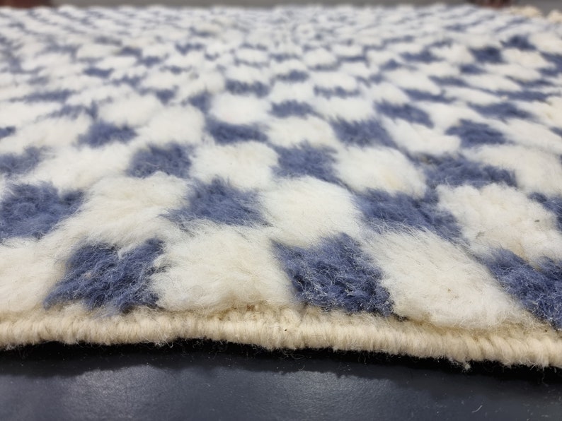Op de afbeelding: Close-up van een wit en blauw pluche tapijt met een geruit patroon. Het tapijt heeft een witte rand.