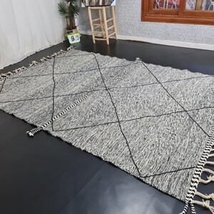 May include: A black and white diamond patterned rug with fringe on all sides. The rug is made of a soft, woven material.