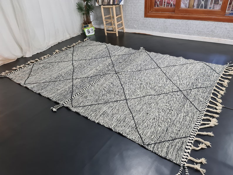May include: A black and white diamond patterned rug with fringe on all sides. The rug is made of a soft, woven material.