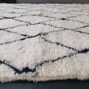 May include: White and black Moroccan rug with a diamond pattern. The rug is made of wool and has a soft, fluffy texture.