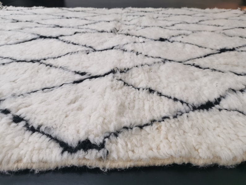 May include: White and black Moroccan rug with a diamond pattern. The rug is made of wool and has a soft, fluffy texture.