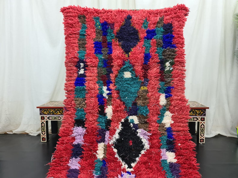 May include: A red, blue, green, and black Moroccan rug with a geometric pattern. The rug is made of wool and has a soft, fluffy texture.