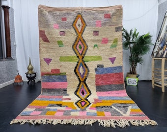 May include: A colorful Moroccan rug with geometric patterns in shades of pink, blue, green, yellow, and black. The rug has a white background and a fringe border.