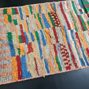 May include: A colorful Moroccan rug with a geometric pattern in shades of red, orange, blue, green, and beige. The rug is handwoven and has a soft, textured surface.