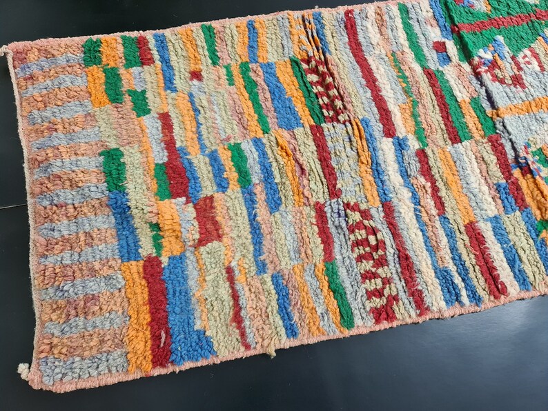 May include: A colorful Moroccan rug with a geometric pattern in shades of red, orange, blue, green, and beige. The rug is handwoven and has a soft, textured surface.