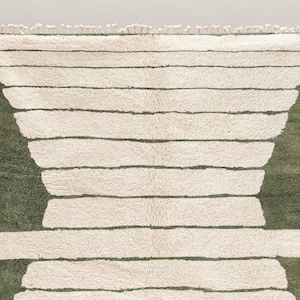 May include: A rectangular rug with a cream-colored background and horizontal olive green stripes. The rug has a geometric design with a fringe at the top. The rug's design features a series of horizontal stripes and a curved shape on each side.