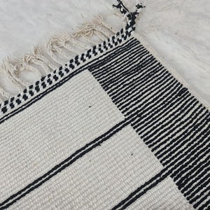May include: A white and black striped rug with fringe. The rug has a geometric pattern with black stripes on a white background.