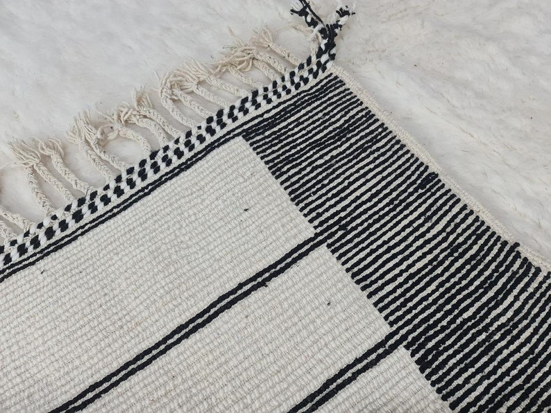 May include: A white and black striped rug with fringe. The rug has a geometric pattern with black stripes on a white background.