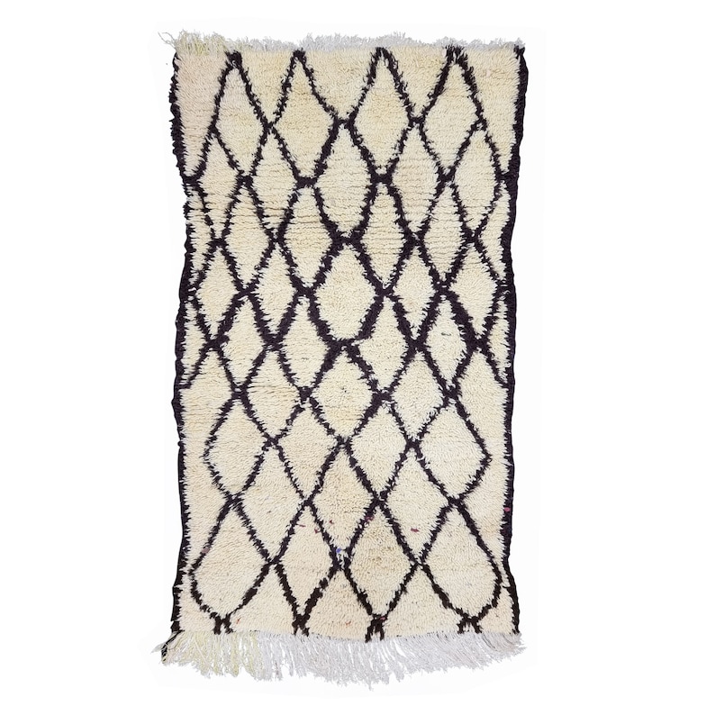 May include: A white and brown Moroccan rug with a diamond pattern. The rug has a fringe border.