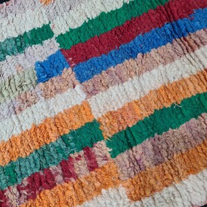 May include: A colorful striped rug with a textured, fuzzy surface. The rug features stripes of green, red, blue, orange, and white.