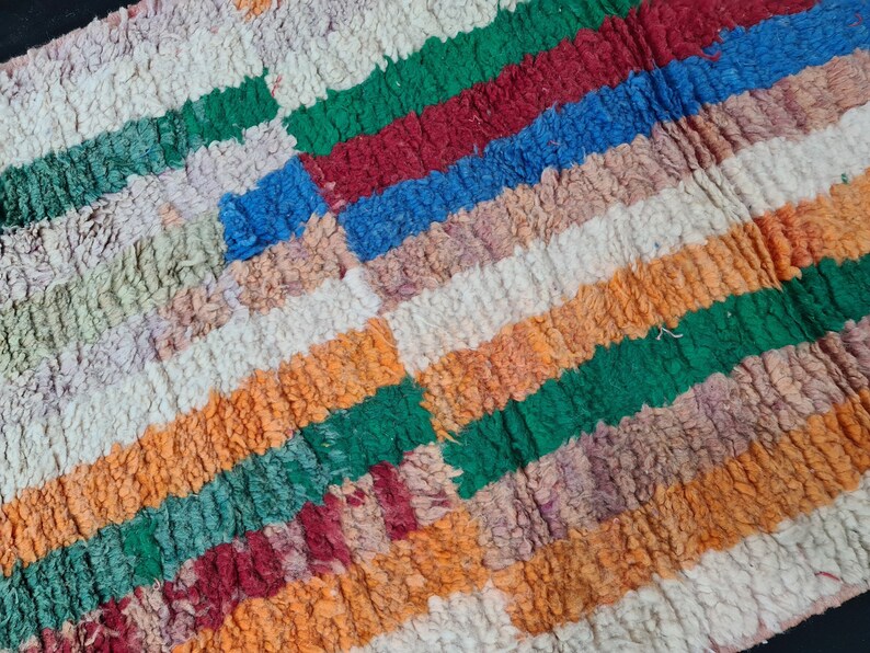 May include: A colorful striped rug with a textured, fuzzy surface. The rug features stripes of green, red, blue, orange, and white.