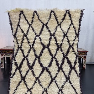 May include: A white and brown Moroccan rug with a diamond pattern. The rug is made of wool and has a soft, fluffy texture.