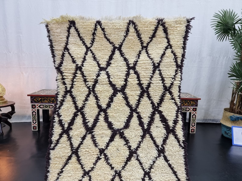 May include: A white and brown Moroccan rug with a diamond pattern. The rug is made of wool and has a soft, fluffy texture.