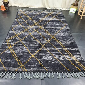 May include: A black and white rug with a geometric pattern of yellow lines. The rug has a fringe border.
