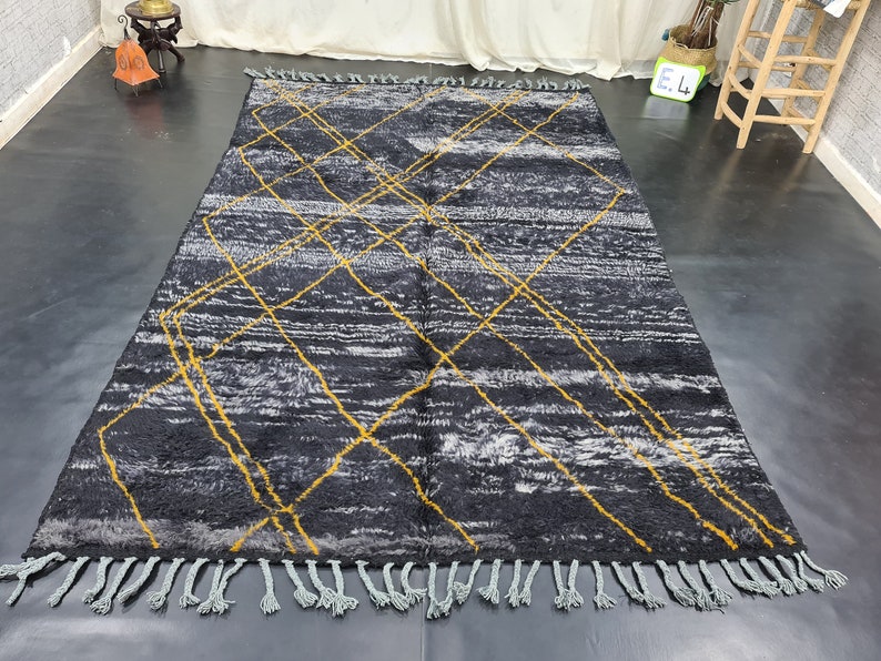 May include: A black and white rug with a geometric pattern of yellow lines. The rug has a fringe border.