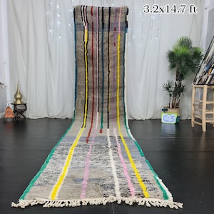Puede incluir: Una alfombra larga y estrecha, tejida a mano, con un patrón de rayas en tonos de gris, rosa, amarillo, verde y azul. La alfombra tiene flecos en ambos extremos y mide 3,2 x 14,7 pies.