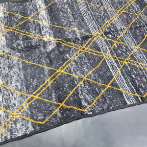 May include: A gray and white rug with yellow geometric lines. The rug has a fringe border.