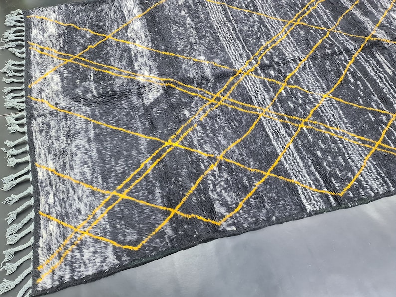 May include: A gray and white rug with yellow geometric lines. The rug has a fringe border.
