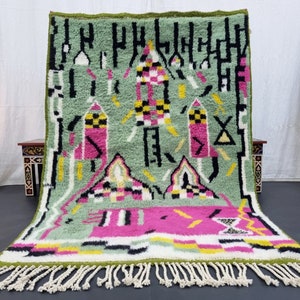 Puede incluir: Una alfombra marroquí verde, rosa, amarilla y negra con un patrón geométrico. La alfombra tiene un borde de flecos.
