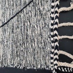 May include: Black and white woven rug with a fringe border. The rug has a textured, hand-woven look.