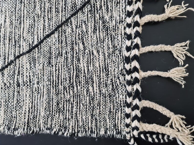 May include: Black and white woven rug with a fringe border. The rug has a textured, hand-woven look.