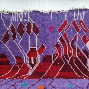 May include: A purple and red Moroccan rug with a geometric pattern. The rug has a fringe border and is made of wool.