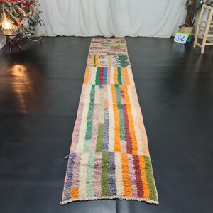 May include: A long, colorful rug with a striped pattern in shades of orange, pink, green, blue, and purple. The rug has a geometric design in the center.