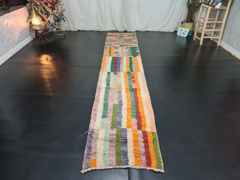 May include: A long, colorful rug with a striped pattern in shades of orange, pink, green, blue, and purple. The rug has a geometric design in the center.