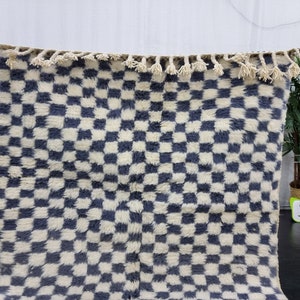 Op de afbeelding: Een wit en blauw geruit tapijt met een franje rand. Het tapijt is gemaakt van een zacht, pluche materiaal.