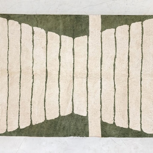 May include: A rectangular rug with a green and cream color scheme. The rug features a central green section with vertical cream-colored stripes. The rug has a textured appearance and a fringed edge, suitable for home decor.