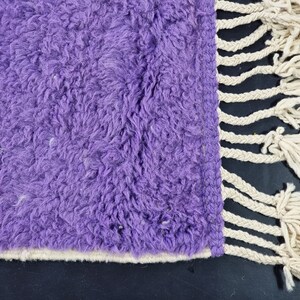 May include: Purple shaggy rug with a white fringe border. The rug has a soft, fluffy texture.