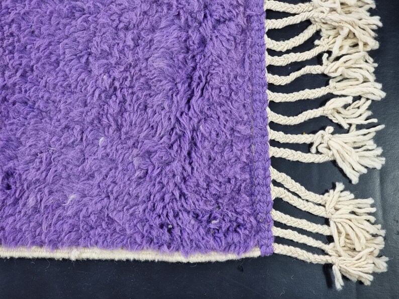 May include: Purple shaggy rug with a white fringe border. The rug has a soft, fluffy texture.