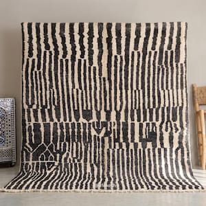 May include: A large, rectangular rug with a black and white striped pattern. The rug has a thick, textured pile and a fringe along the bottom edge. A decorative mosaic fountain and a wooden chair are in the background.