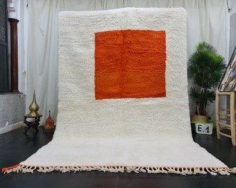 May include: A white shag rug with a large orange square in the center. The rug has a fringe border.