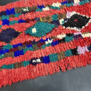 May include: A colorful Moroccan rug with a red background and a variety of geometric patterns in shades of blue, green, purple, and white.