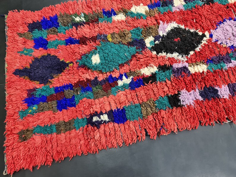 May include: A colorful Moroccan rug with a red background and a variety of geometric patterns in shades of blue, green, purple, and white.
