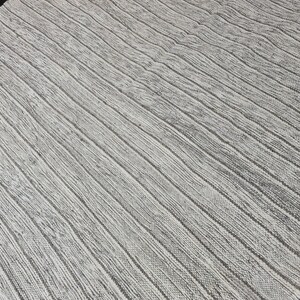 Puede incluir: Una alfombra blanca tejida con un patr&oacute;n texturizado a rayas. La alfombra tiene un brillo sutil y una textura ligeramente rugosa.