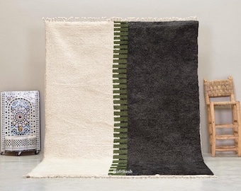 May include: A large, rectangular rug with a cream-coloured section on the left and a dark grey section on the right. A vertical stripe of olive green and white rectangles divides the two sections. The rug has a shaggy texture and a fringed edge.