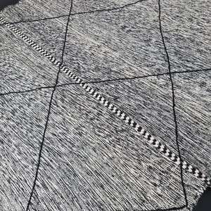 May include: Black and white diamond patterned rug with fringe tassels on the ends. The rug has a woven texture.