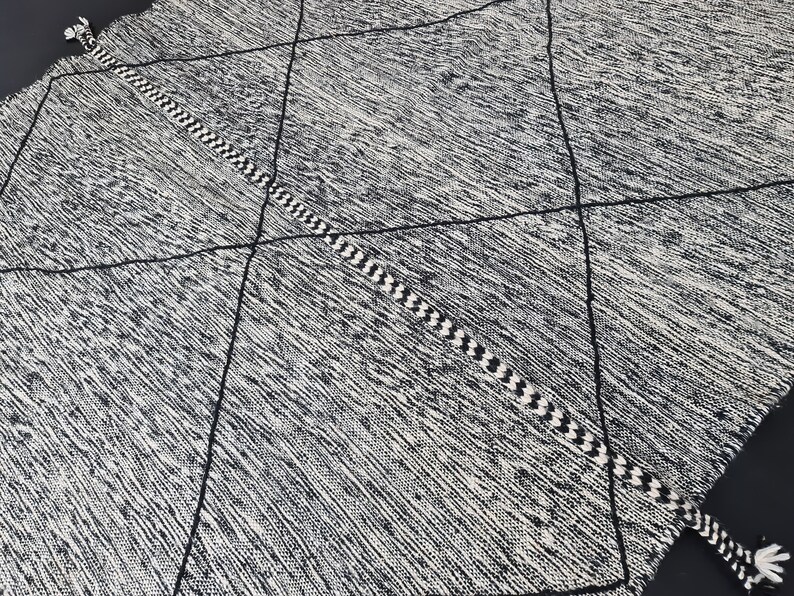May include: Black and white diamond patterned rug with fringe tassels on the ends. The rug has a woven texture.