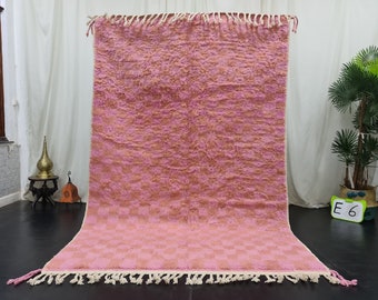 May include: A pink and orange Moroccan rug with a checkered pattern and fringe. The rug is hanging on a white wall.