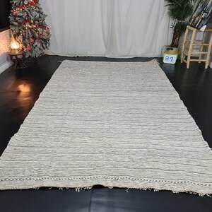 Puede incluir: Una alfombra rayada blanca y gris con un borde de flecos. La alfombra est&aacute; hecha de un material suave y texturizado.