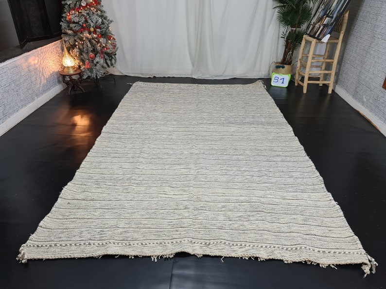 Puede incluir: Una alfombra rayada blanca y gris con un borde de flecos. La alfombra est&aacute; hecha de un material suave y texturizado.