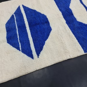 Puede incluir: Una alfombra blanca con un patr&oacute;n geom&eacute;trico azul. La alfombra tiene un borde de flecos.