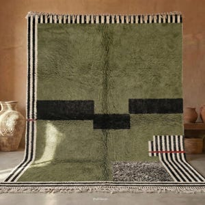 May include: A large rectangular rug with a deep olive green shaggy pile. The design features bold black horizontal blocks, a section of black and white stripes, and a small red horizontal line accent. The edges are finished with white fringe.