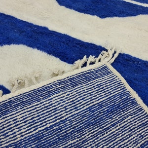 Puede incluir: Primer plano de una alfombra rayada azul y blanca con flecos. La alfombra tiene una textura tejida y est&aacute; hecha de fibras suaves.