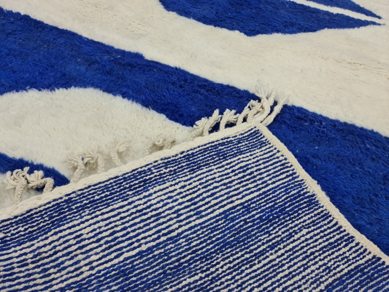 Puede incluir: Primer plano de una alfombra rayada azul y blanca con flecos. La alfombra tiene una textura tejida y est&aacute; hecha de fibras suaves.