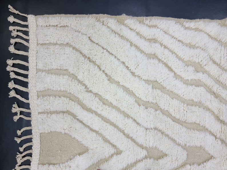 May include: A white and beige rug with a wavy, abstract pattern. The rug has a fringe border.