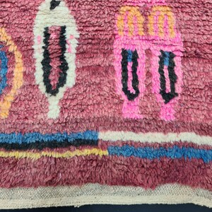 May include: Close-up of a pink, white, blue, and orange patterned rug with a fringe border. The rug has a textured, woven look.